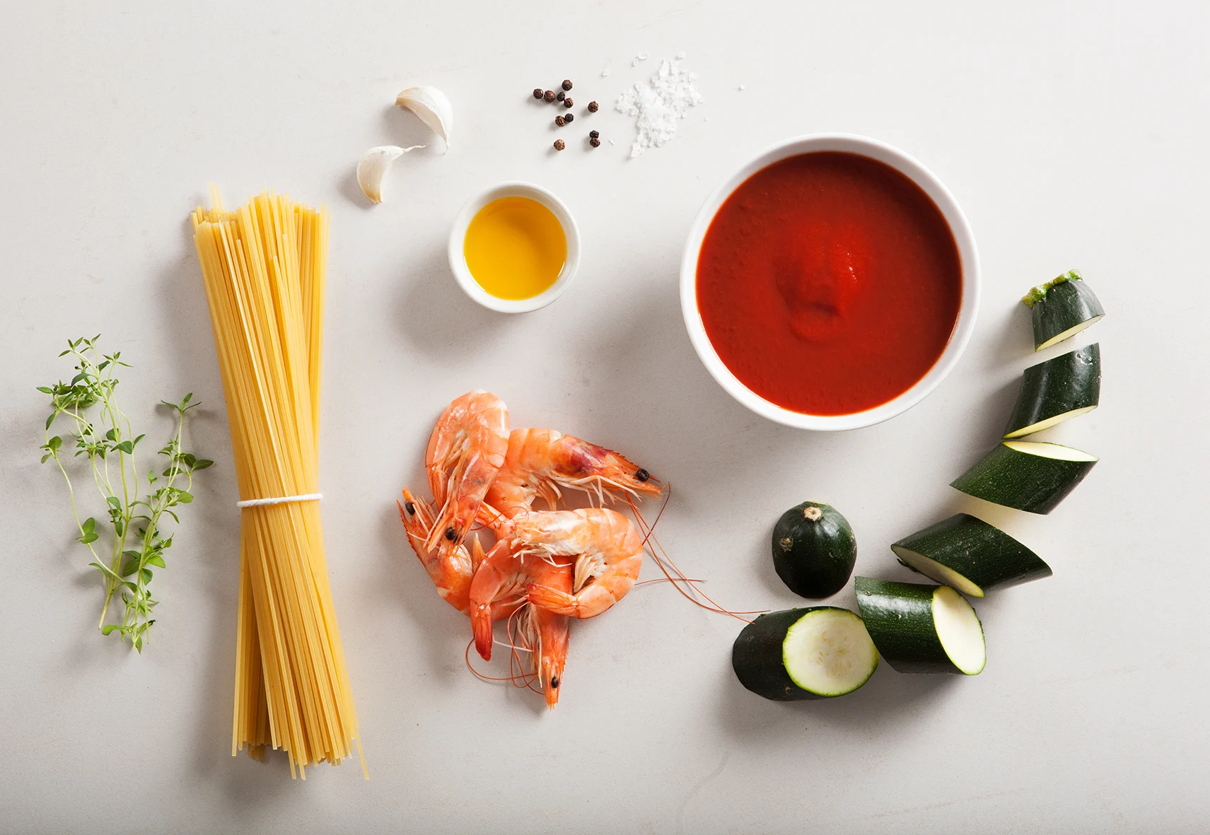 Makaron spaghetti, krewetki, cukinia i sos pomidorowy na jasnym tle